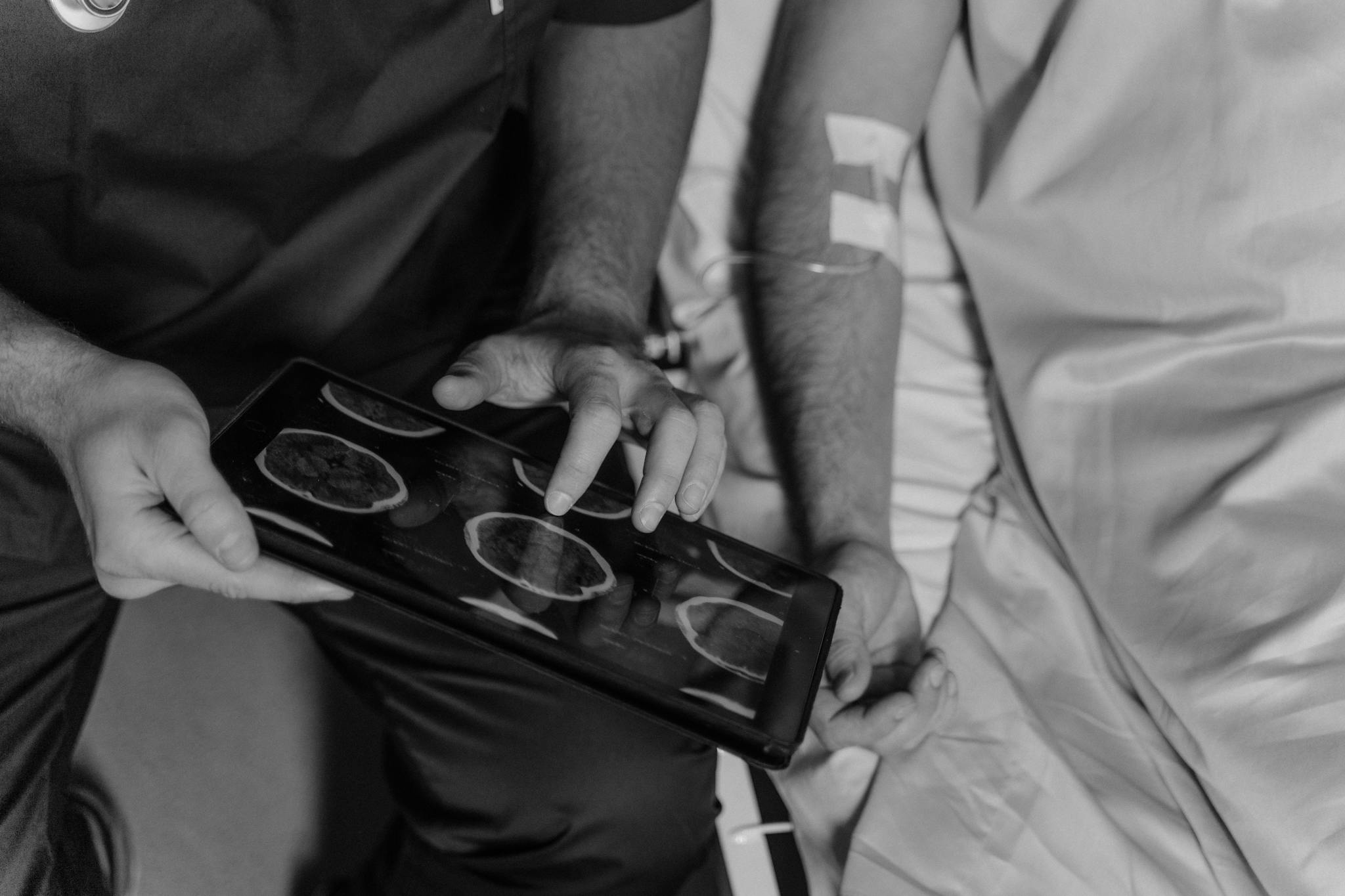 Medical professional reviews patient's CT scans on a digital tablet in grayscale.