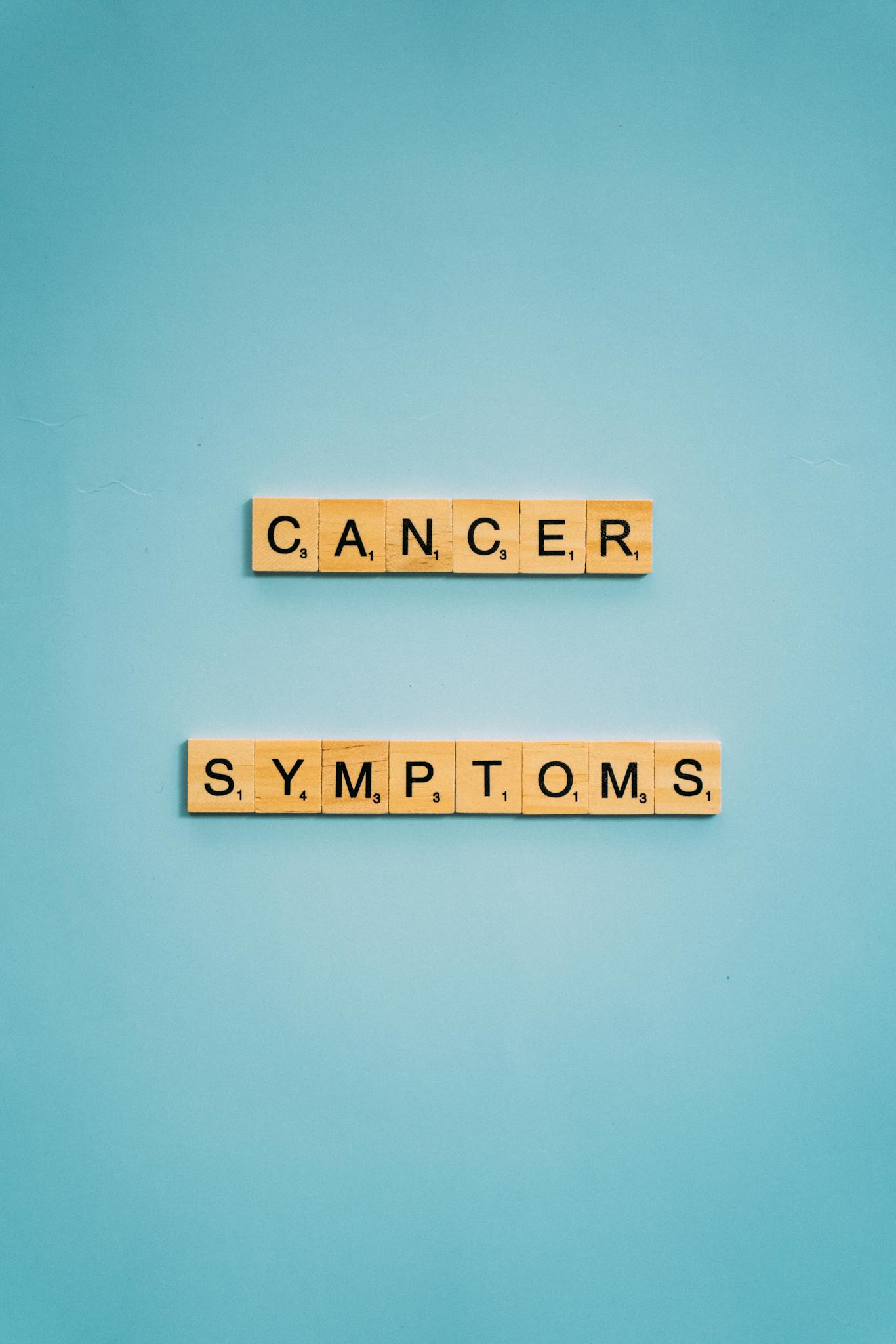 Scrabble tiles spelling 'cancer symptoms' on a blue background, emphasizing awareness.