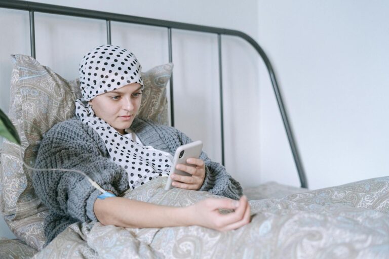 Woman in bed undergoing cancer treatment, looking at her phone with hope and determination.